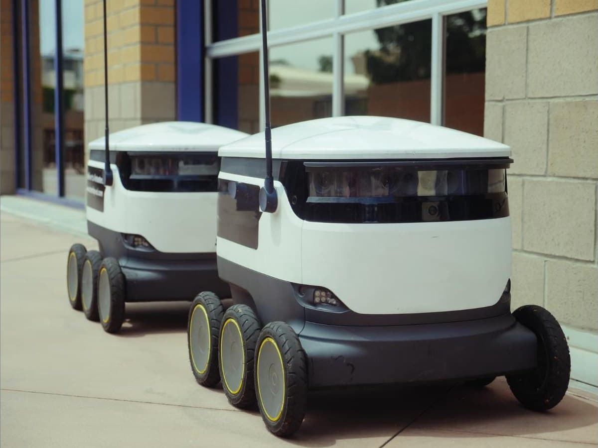 Two autonomous delivery robots on a walkway outside a building